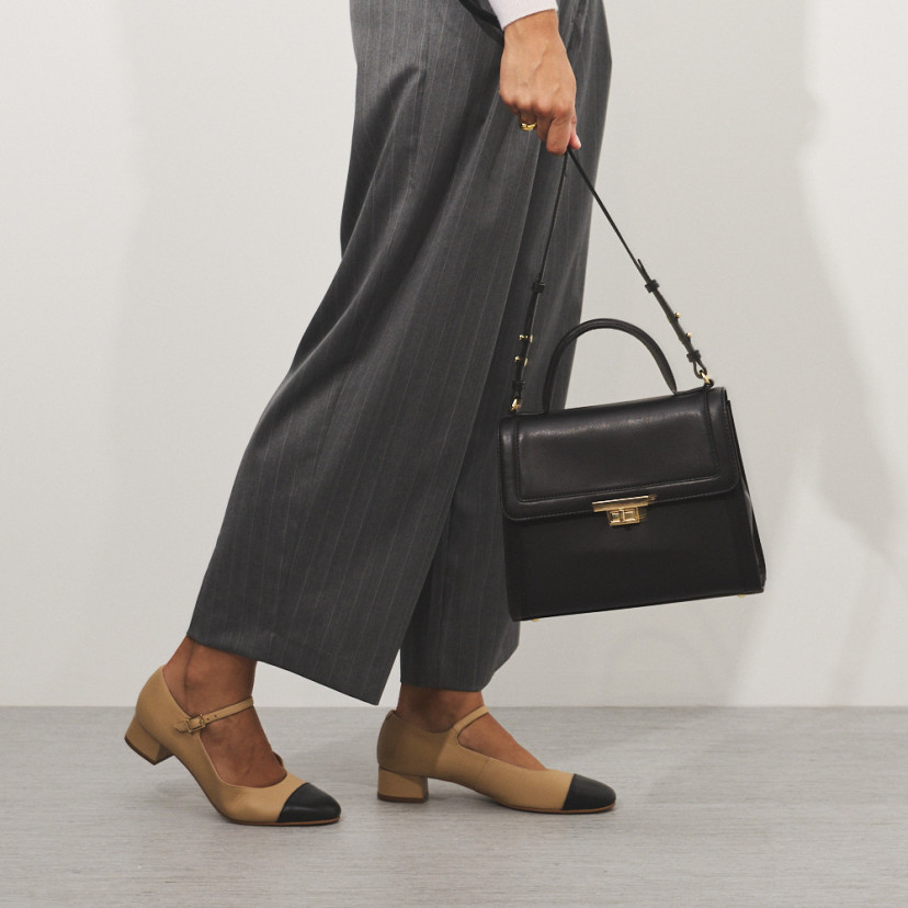 Bolsa de couro feminina anos 60 na cor preta com vista frontal, segurada pela alça longa, bolsa em movimento - MONPIEL