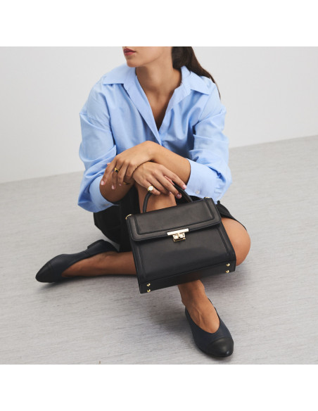 Schwarze Lederhandtasche im 60er-Stil für Damen, auf dem Bein abgelegt mit Ballerina-Detail - MONPIEL