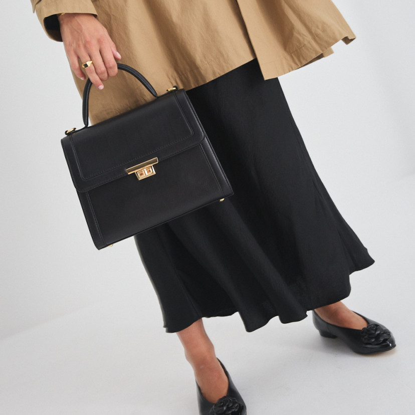 Black 60's women's leather handbag with front view, held in hand by the short handle, with ballerinas featuring floral - MONPIEL