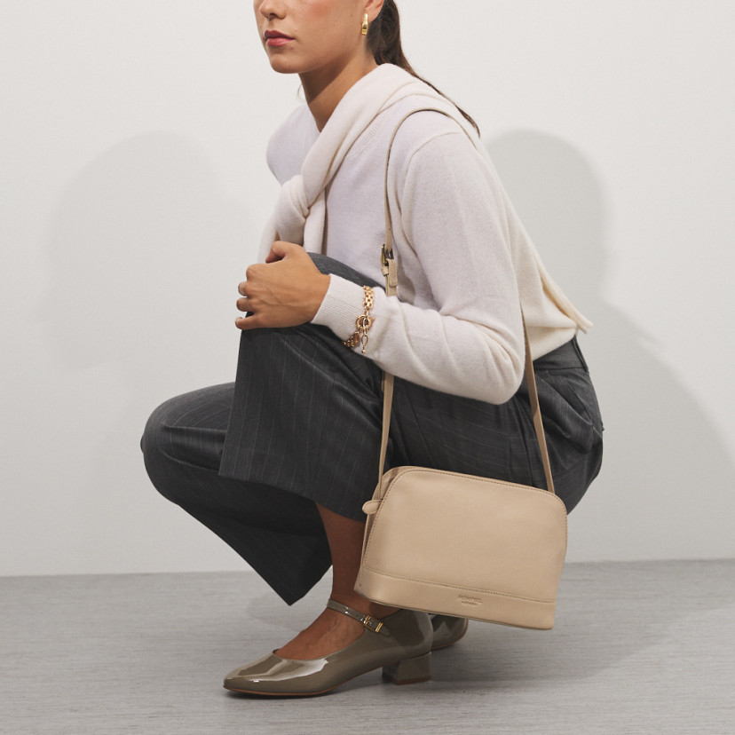 Medium beige leather handbag hanging from the shoulder with the model crouching - MONPIEL