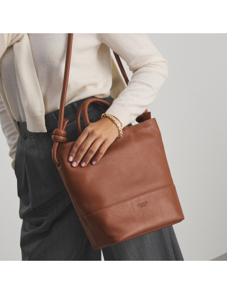 Large leather knot handbag in leather color, hanging from the shoulder with perspective view - MONPIEL Large leather knot handbag in leather color, hanging from the shoulder with perspective view - MONPIEL