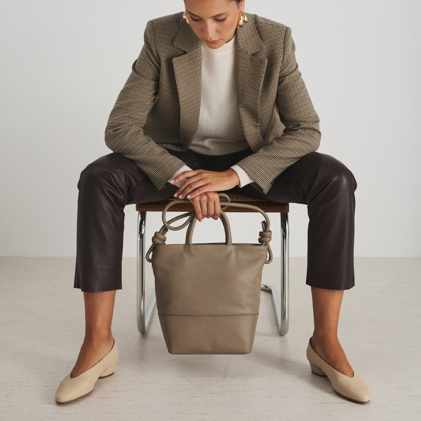 Large taupe leather knot handbag with front view, hanging from the hands - MONPIEL