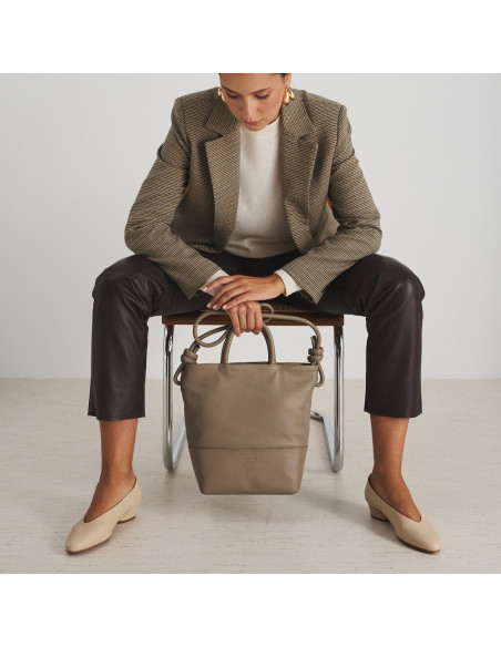 Large taupe leather knot handbag with front view, hanging from the hands - MONPIEL Large taupe leather knot handbag with front view, hanging from the hands - MONPIEL