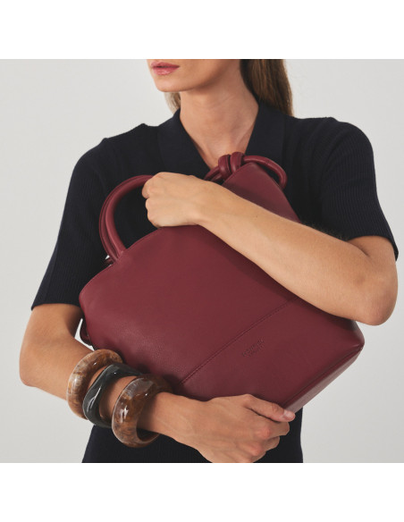 Large burgundy leather knot handbag with the model holding the bag with both arms - MONPIEL Large burgundy leather knot handbag with the model holding the bag with both arms - MONPIEL