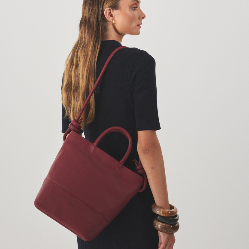 Large burgundy leather knot handbag hanging from the shoulder with the model in profile - MONPIEL