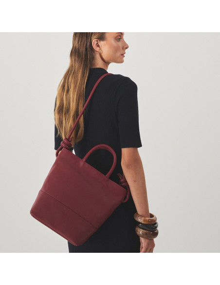 Large burgundy leather knot handbag hanging from the shoulder with the model in profile - MONPIEL Large burgundy leather knot handbag hanging from the shoulder with the model in profile - MONPIEL