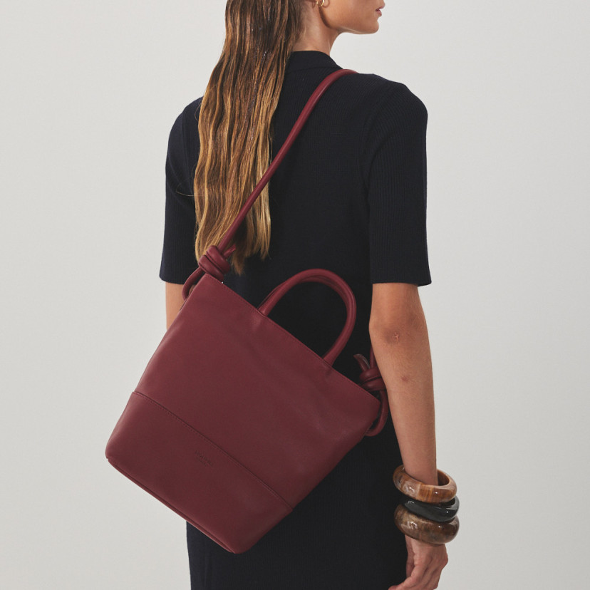 Large burgundy leather knot handbag hanging from the shoulder with the model carrying the bag on the back - MONPIEL