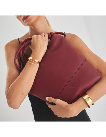 Large burgundy leather knot handbag tilted, with the model holding it in her arms - MONPIEL Large burgundy leather knot handbag tilted, with the model holding it in her arms - MONPIEL