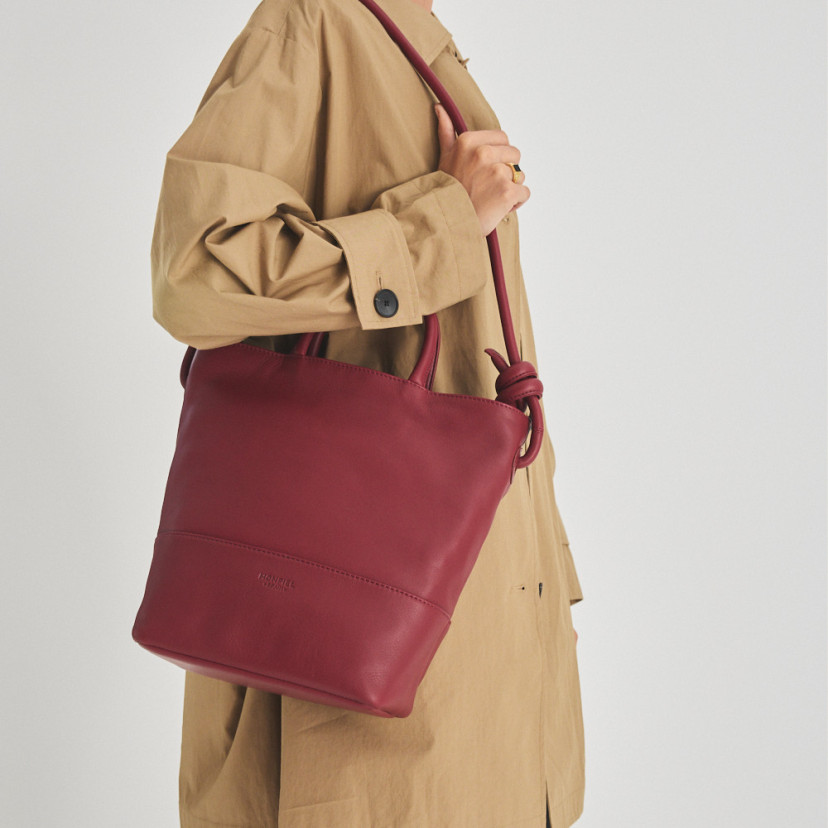 Grande bolsa de couro com nós na cor bordô, pendurada no ombro com o modelo de perfil - MONPIEL