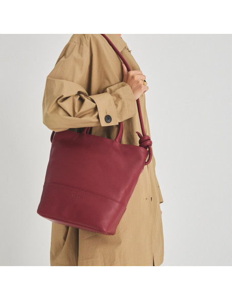 Grande bolsa de couro com nós na cor bordô, pendurada no ombro com o modelo de perfil - MONPIEL