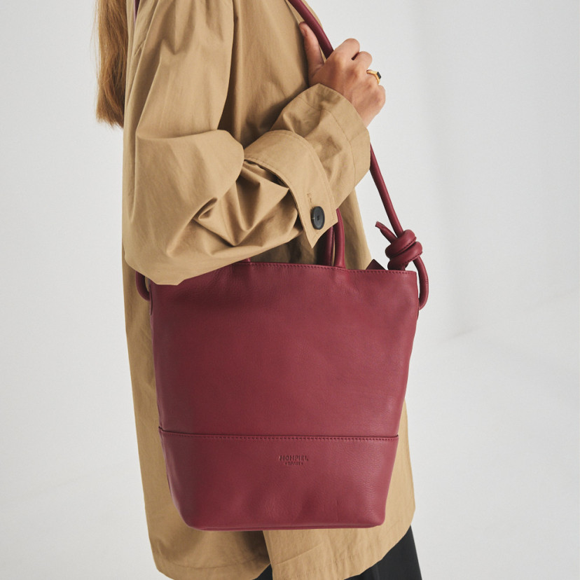 Grande bolsa de couro com nós na cor bordô, pendurada no ombro com o modelo de perfil e vista frontal da bolsa - MONPIEL