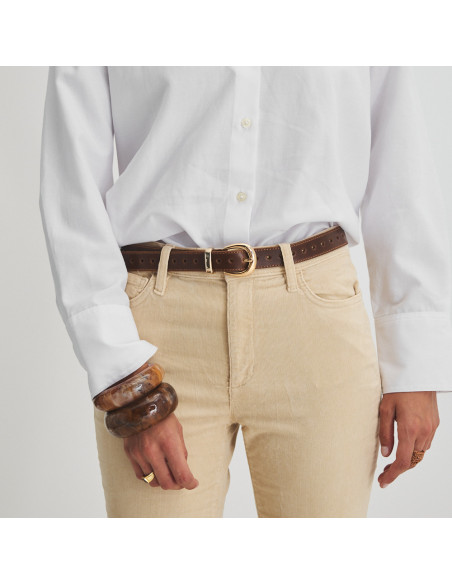 Cinturino in pelle con cuori color cuoio, vista frontale, su pantaloni beige di velluto a coste e camicia bianca, prim - MONPIEL