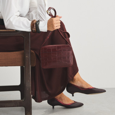 Bolsa de couro croco na cor couro com alça de bandoleira segurada com as mãos, vista frontal - MONPIEL 2