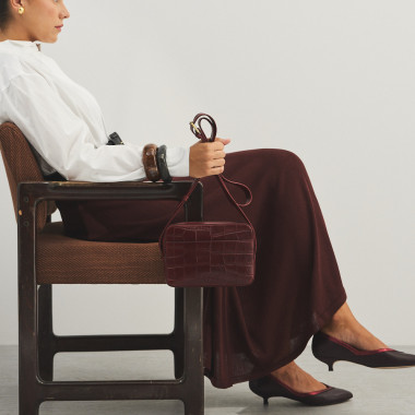 Crocodile leather crossbody bag in brown, with crossbody handle held with hands, front view - MONPIEL 2