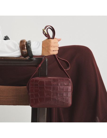 Bolsa a tiracolo de couro bordô com estampa de crocodilo segurada pela alça longa com vista frontal e close-up - MONPIEL Bolsa a tiracolo de couro bordô com estampa de crocodilo segurada pela alça longa com vista frontal e close-up - MONPIEL
