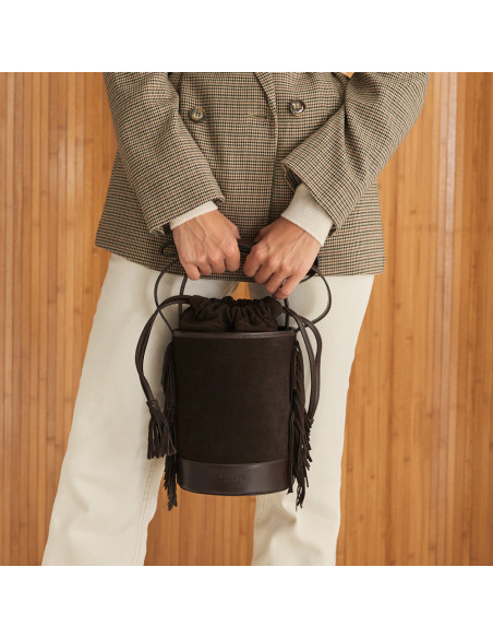 Small Roma leather fringe bucket bag in brown suede, front view, held with both hands by the short handle - MONPIEL