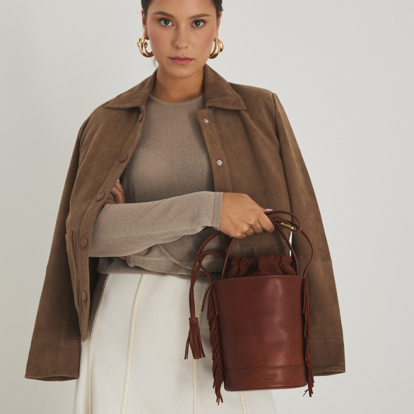 Small Roma leather fringe bucket bag in leather color, front view, held by the short handle - MONPIEL