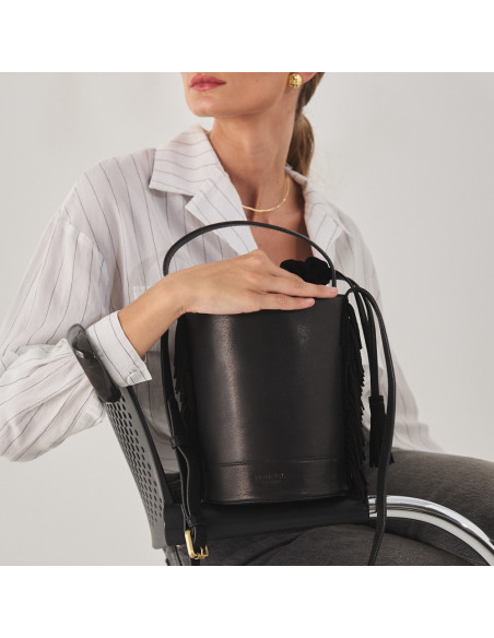 Small Roma leather fringe bucket bag in black, front view, resting on the armrest - MONPIEL