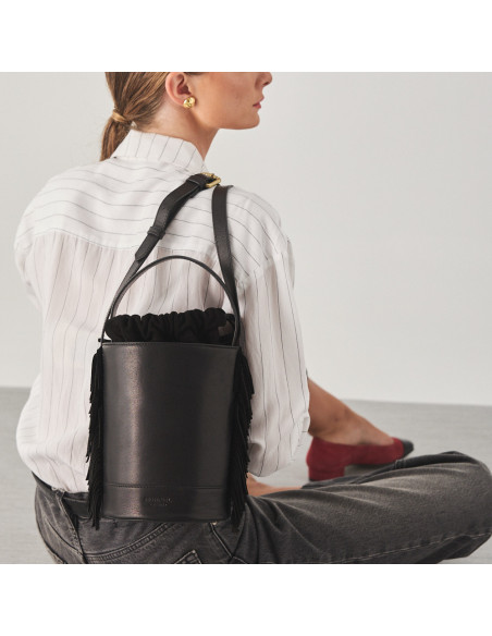Petit sac seau Roma avec franges en cuir noir, porté sur le dos, avec modèle assis par terre - MONPIEL