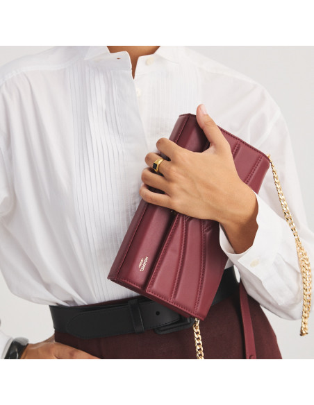 Clutch de couro feminino Venecia em cor bordô, segurado na mão, inclinado, close-up - MONPIEL