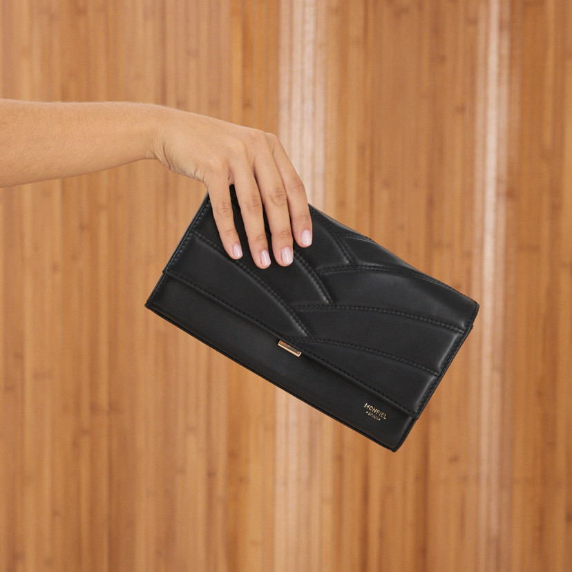 Clutch de couro feminino Venecia em cor preta, vista frontal, segurado na mão - MONPIEL