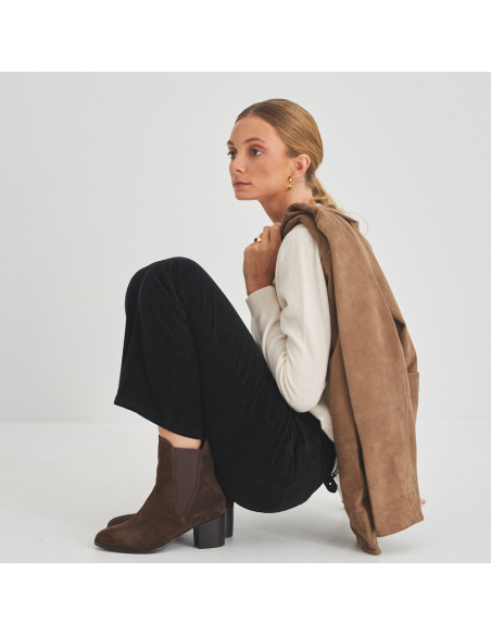Bota de couro Marcela em camurça marrom, vista de perfil de modelo agachada com jaqueta nos ombros - MONPIEL Bota de couro Marcela em camurça marrom, vista de perfil de modelo agachada com jaqueta nos ombros - MONPIEL
