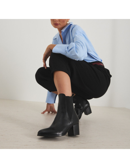 Marcela-Lederstiefelette in Schwarz, Perspektivansicht des Stiefels, Modell hockend mit ausgestrecktem Bein - MONPIEL Marcela-Lederstiefelette in Schwarz, Perspektivansicht des Stiefels, Modell hockend mit ausgestrecktem Bein - MONPIEL