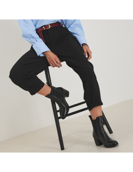 Bota de couro Marcela em cor preta, plano médio, modelo sentado em banqueta com o pé apoiado - MONPIEL Bota de couro Marcela em cor preta, plano médio, modelo sentado em banqueta com o pé apoiado - MONPIEL