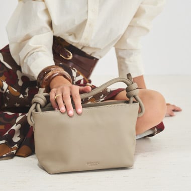 Bolsa pequena de couro com nós na cor taupe, vista frontal e detalhe da alça, apoiada sobre uma rocha - MONPIEL 2