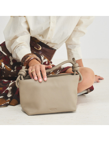 Petit sac noué en cuir taupe, posé au sol, tenu par une main, vue de face - MONPIEL