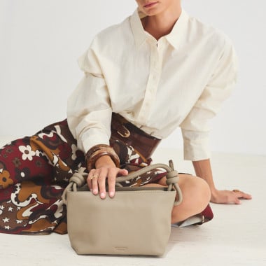 Bolsa pequena de couro com nós na cor taupe, vista frontal e detalhe da alça, apoiada sobre uma rocha - MONPIEL 2