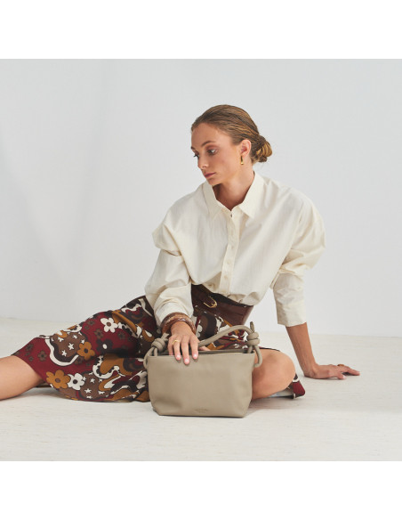 Piccola borsa a nodi in pelle color talpa, modello seduto sul pavimento con una mano appoggiata sulla borsa, vista gen - MONPIEL