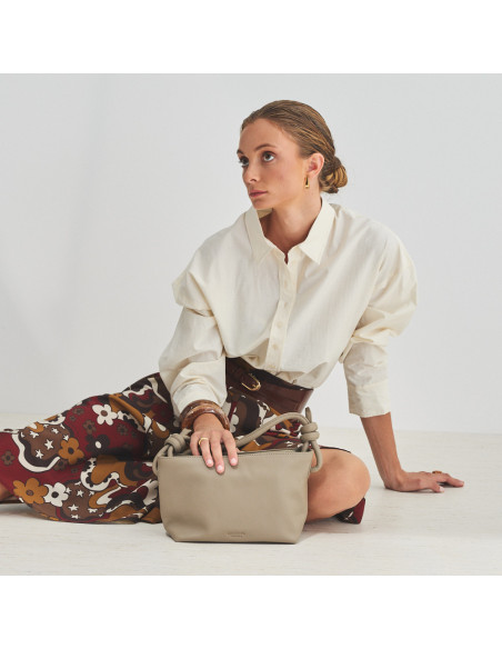 Petit sac noué en cuir taupe, modèle assis par terre avec la main posée sur le sac, vue générale - MONPIEL