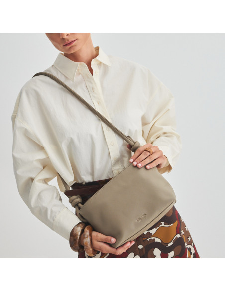 Bolsa de couro com nós pequena na cor taupe pendurada no ombro e segurada com as mãos, vista frontal e inclinada da bo - MONPIEL