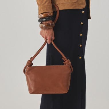 Bolsa pequena de couro com nós na cor taupe, vista frontal e detalhe da alça, apoiada sobre uma rocha - MONPIEL 2