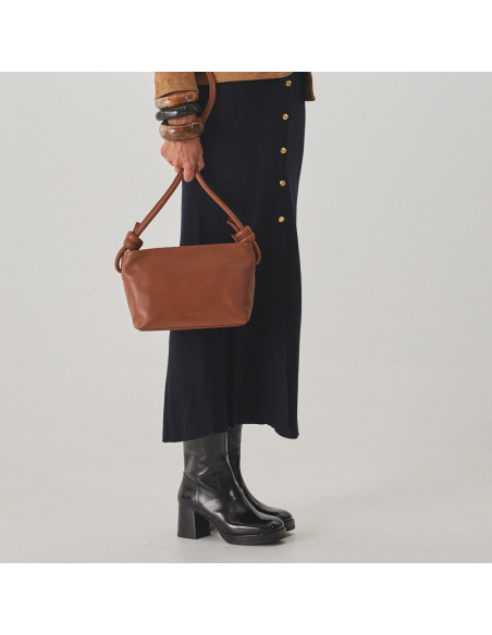 Bolsa de couro com nós pequena na cor couro, segurando as alças com a mão, vista frontal da bolsa, plano médio - MONPIEL