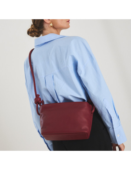 Bolsa de couro com nós pequena na cor bordô, pendurada no ombro, vista das costas do modelo - MONPIEL