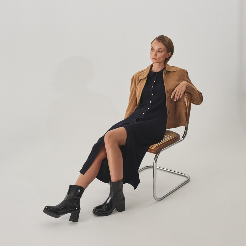 Jaqueta de couro feminina com costuras na cor camelo, vista em perspectiva, plano geral da modelo sentada na cadeira - MONPIEL