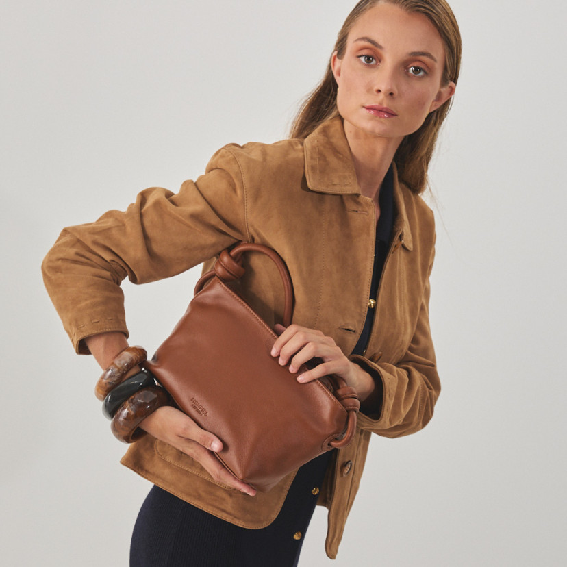 Jaqueta de couro feminina com costuras na cor camelo, vista de perfil, com bolsa de couro na mão - MONPIEL