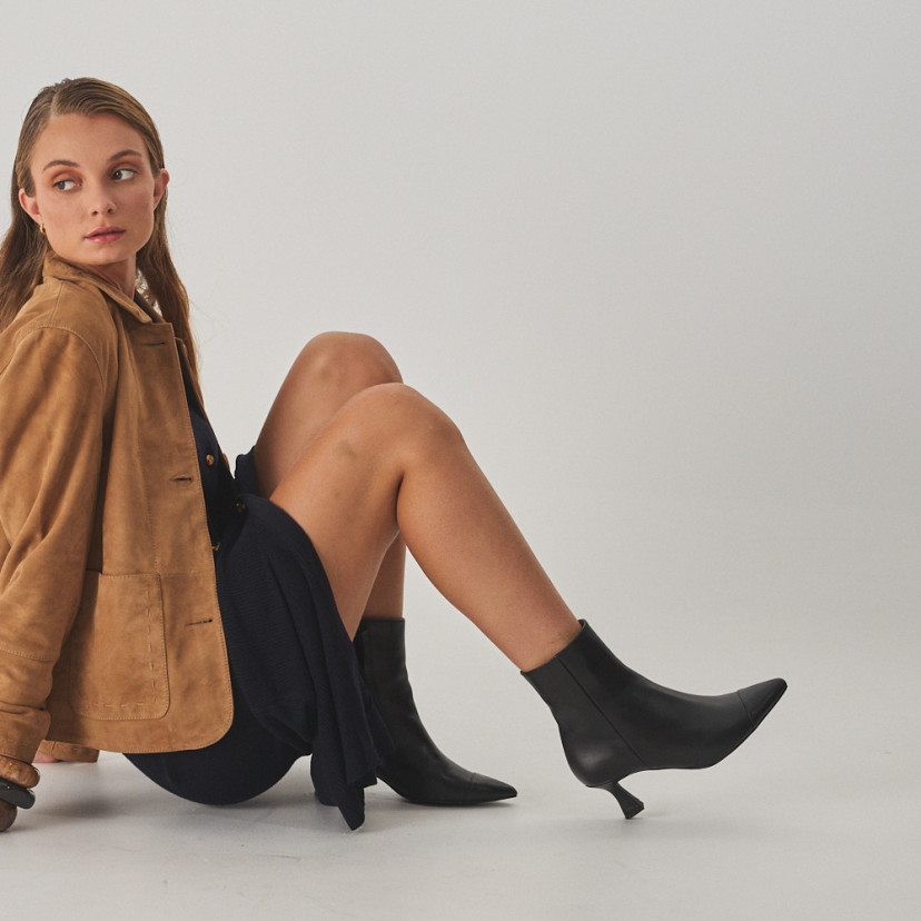 Jimena pointed-toe leather ankle boot in black, side view, full shot of the model sitting on the floor - MONPIEL