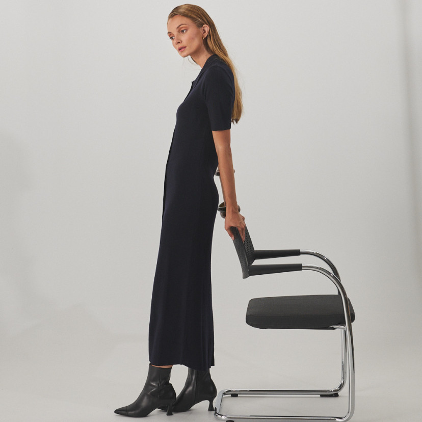 Jimena pointed-toe leather ankle boot in black, side view, full shot of model standing with support from the chair - MONPIEL