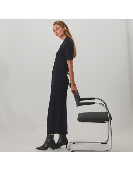 Jimena black leather pointed-toe ankle boot, profile view, wide shot of model standing, leaning on a chair - MONPIEL Jimena black leather pointed-toe ankle boot, profile view, wide shot of model standing, leaning on a chair - MONPIEL
