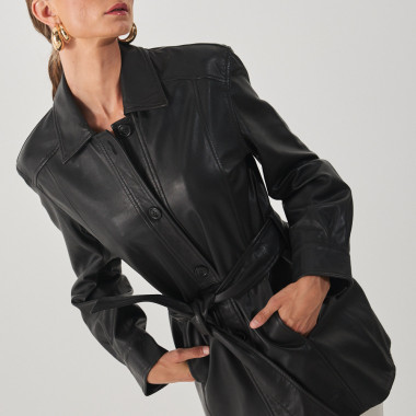Trench de couro preto, modelo apoiada na parede com as mãos na cintura - MONPIEL 2