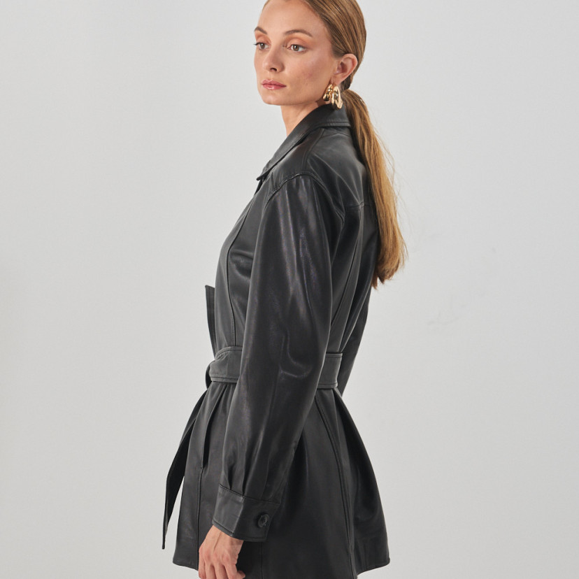 Black leather trench coat, side view against a white wall - MONPIEL