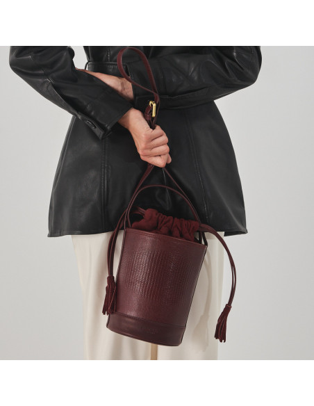 Small round bucket leather bag in burgundy snake print, front view, held at the back - MONPIEL
