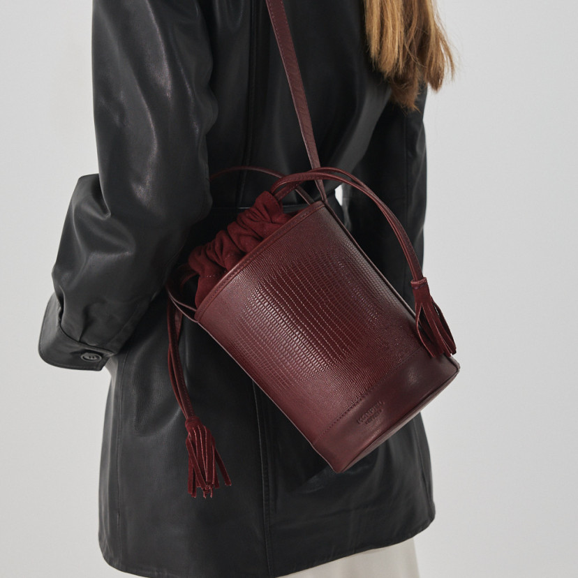 Bolsa bucket redonda pequena de couro em cor de serpente bordô, pendurada no ombro - MONPIEL