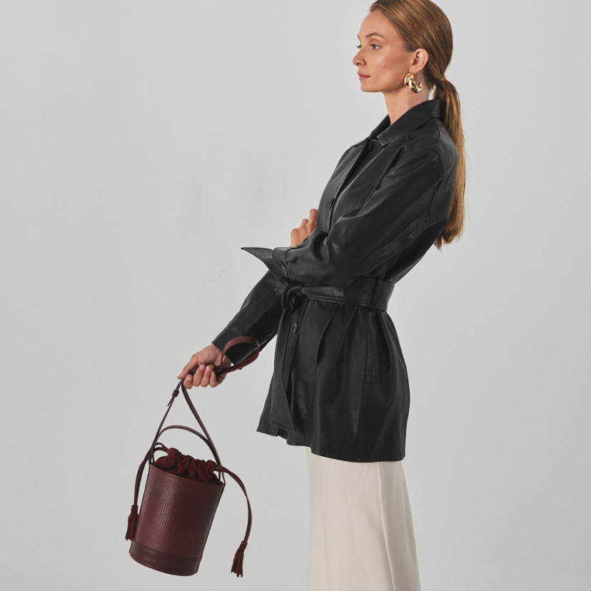 Small round bucket leather bag in burgundy snake print, held by the long strap, bag in motion - MONPIEL