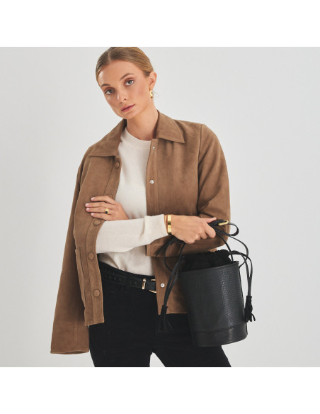 Bolsa bucket redonda pequena de couro em cor de serpente preta, vista frontal, segurada pelas mãos na alça - MONPIEL