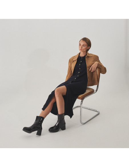 Claudia black patent leather platform boot, perspective view, wide shot of model sitting on a chair - MONPIEL Claudia black patent leather platform boot, perspective view, wide shot of model sitting on a chair - MONPIEL
