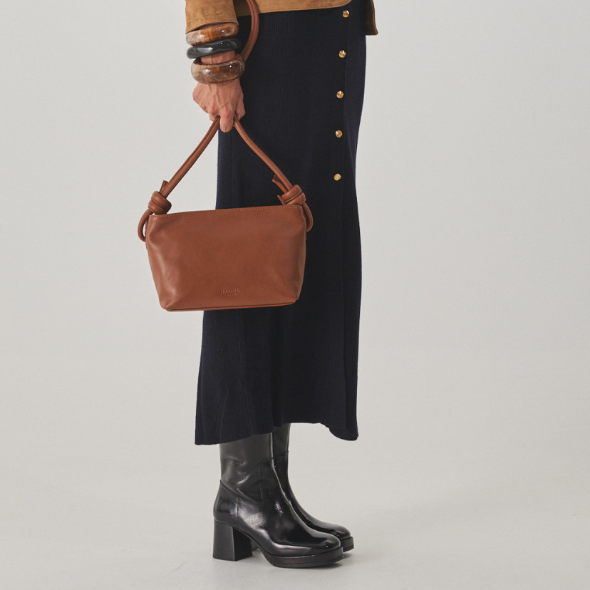 Bota de plataforma Claudia em verniz preto, vista em perspectiva e detalhe de bolsa de couro na mão - MONPIEL